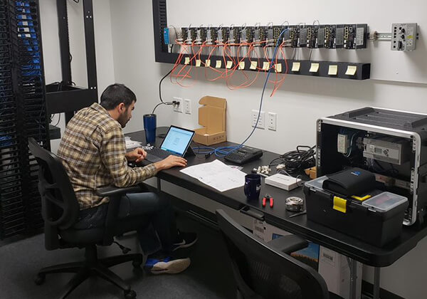 OTCR team member working on bank of network switches with laptop