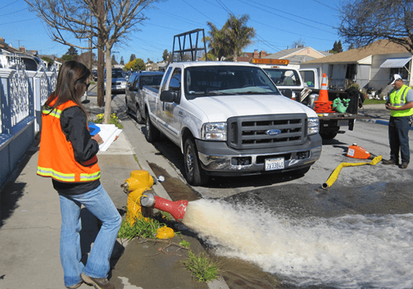 staff performing flushing at a water hydrant in the street